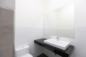 Une salle de bain avec un lavabo blanc, un plan de toilette noir et un grand miroir au-dessus.