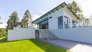 Una casa moderna amb façana de vidre, exterior blanc i un jardí ben cuidat.