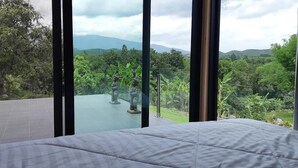 Un dormitorio con una cama grande, vista a un jardín con estatuas y un paisaje montañoso al fondo.