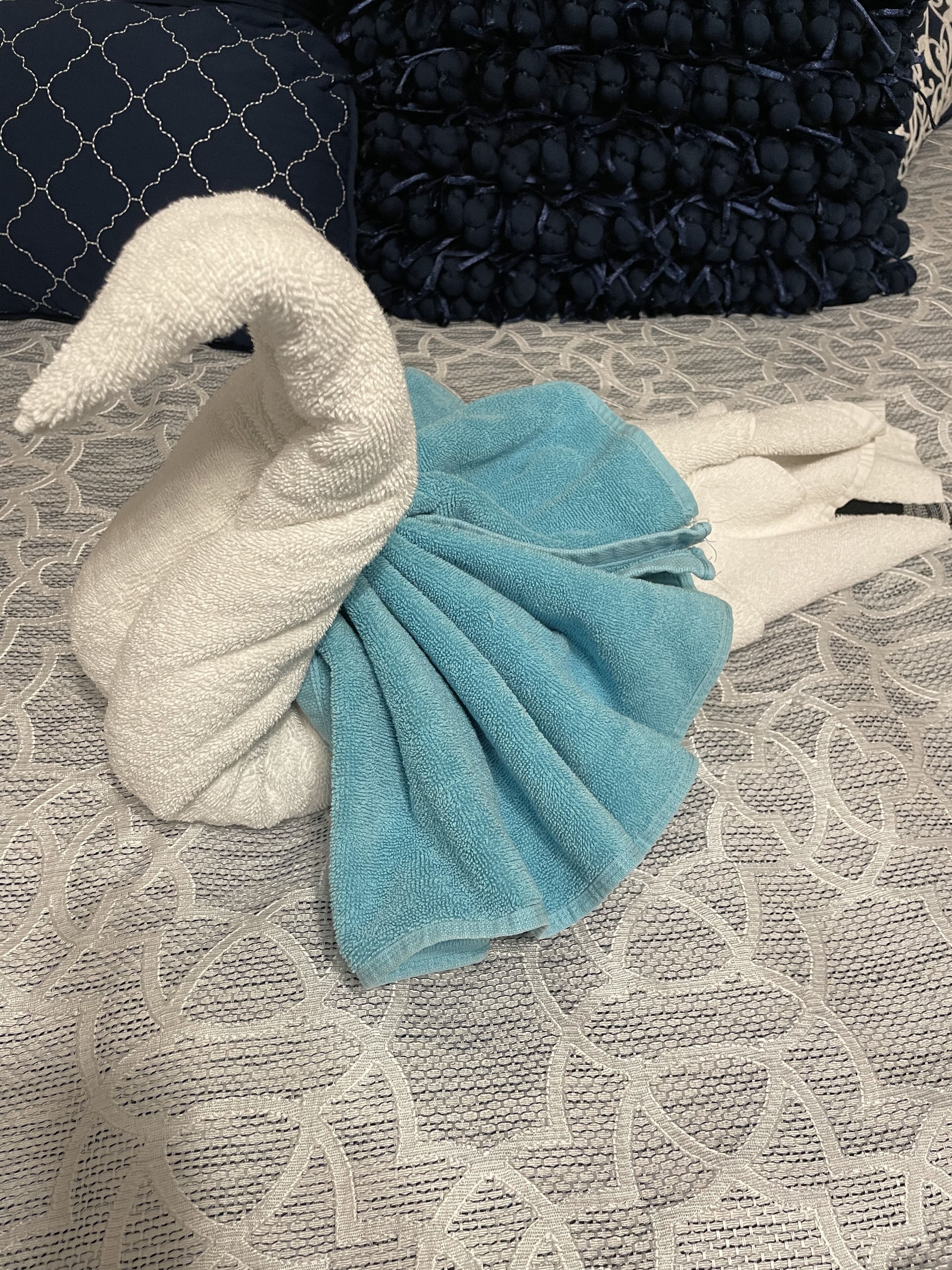 Ein handtuch in Form eines Schwans auf einem Bett mit einem gemusterten Überwurf.