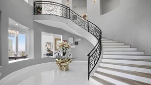 Un intérieur spacieux et moderne, agrémenté d’un escalier en colimaçon, d’une table centrale dotée d’un piétement doré et d’œuvres d’art encadrées qui ornent les murs.