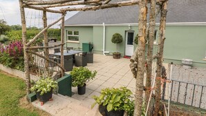 Área de pátio com estrutura de pérgola, assentos externos e plantas em vasos.