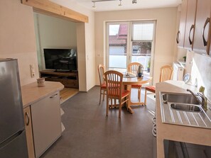 A compact kitchen with a dining area, a built-in TV, and a window with a view of a red-tiled roof.