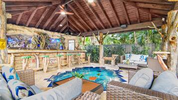Un espace extérieur abrité, aménagé avec des meubles en osier, une piscine et un coin bar décoré en bois.