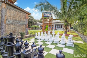 Enjoy a leisurely game of chess on the well-maintained lawn, surrounded by a colorful playhouse and palm trees.