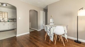 Un coin repas avec une table dressée pour deux personnes, une cuisine en arrière-plan et un couloir menant à une autre pièce.