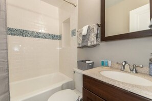Un baño con bañera, inodoro, tocador con lavabo y espejo.