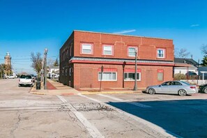 Un edificio de ladrillo de dos pisos con techo rojo, acera y calle con coches estacionados.