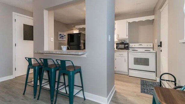 A compact kitchen with a bar area, a refrigerator, a stove, and bar stools. - Welcome to the Lakeside Suite! Enjoy! (Fairport Harbor)