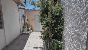 A narrow alleyway with a tiled floor, a white wall on one side, and a metal gate at the end. - Meu cantinho  (Guaratingueta)