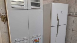 A white refrigerator with a freezer compartment on top, a small window, and a decorative item hanging on the door. - Meu cantinho  (Guaratingueta)