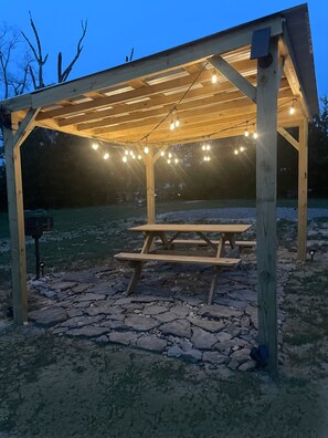 Eine Holzpergola mit Lichterketten und einem Picknicktisch.