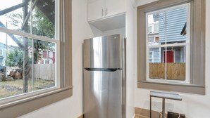 Een kleine keuken met een roestvrijstalen koelkast, witte kastjes en een raam met uitzicht op een achtertuin.