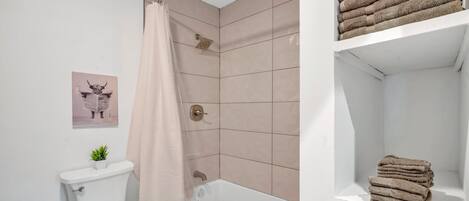 A bathroom with a toilet, shower, and shelves with towels.
