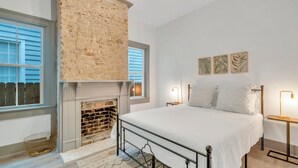 Een slaapkamer met een metselwerk open haard, een groot bed en uitzicht op buiten door een raam.