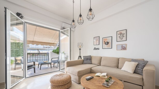 Ein modernes Wohnzimmer mit einem beigefarbenen Ecksofa, einem runden Couchtisch aus Holz und einer Glastür, die auf eine Terrassenanlage mit Tisch und Stühlen führt.