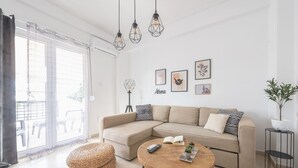 Ein modernes Wohnzimmer mit einem beigefarbenen Ecksofa, einem runden Couchtisch aus Holz und einem großen Fenster mit durchsichtigen Vorhängen.