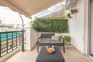 A balcony with a grey sofa, a small table with a bowl of cookies, and potted plants. - Live As A Greek in Athena (Athens)