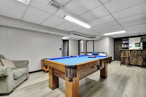 A pool table in a room with a sofa, a dartboard, and a bar area.
