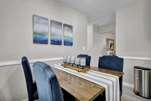 A dining area with a wooden table, blue upholstered chairs, and three abstract paintings on the wall.
