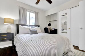 A bedroom with a bed, bedside table, lamp, window with curtains, and a wardrobe.