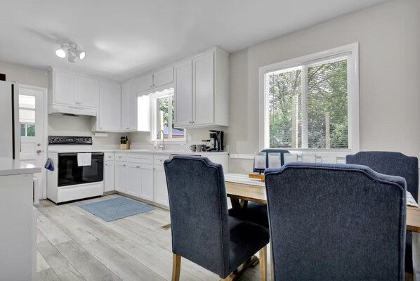 A modern kitchen with white cabinetry, a built-in oven, and a dining area with two chairs.