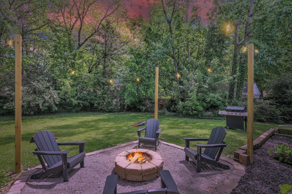 Un jardin avec un foyer, trois fauteuils Adirondack et un barbecue.