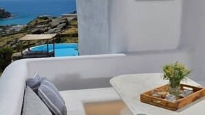 Ett vitt rum med utsikt över havet, ett litet bord och en soffa med kuddar.