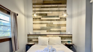 A neatly made bed with white linens and two swan-shaped towels, a wooden headboard with a rustic finish, and two pendant lights hanging above. - Cozy Room for the Budget Traveler in Maya Beach (Maya Beach)