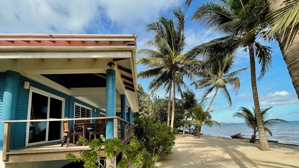 A beachfront property with a covered porch, palm trees, and a sandy beach. - Cozy Room for the Budget Traveler in Maya Beach (Maya Beach)