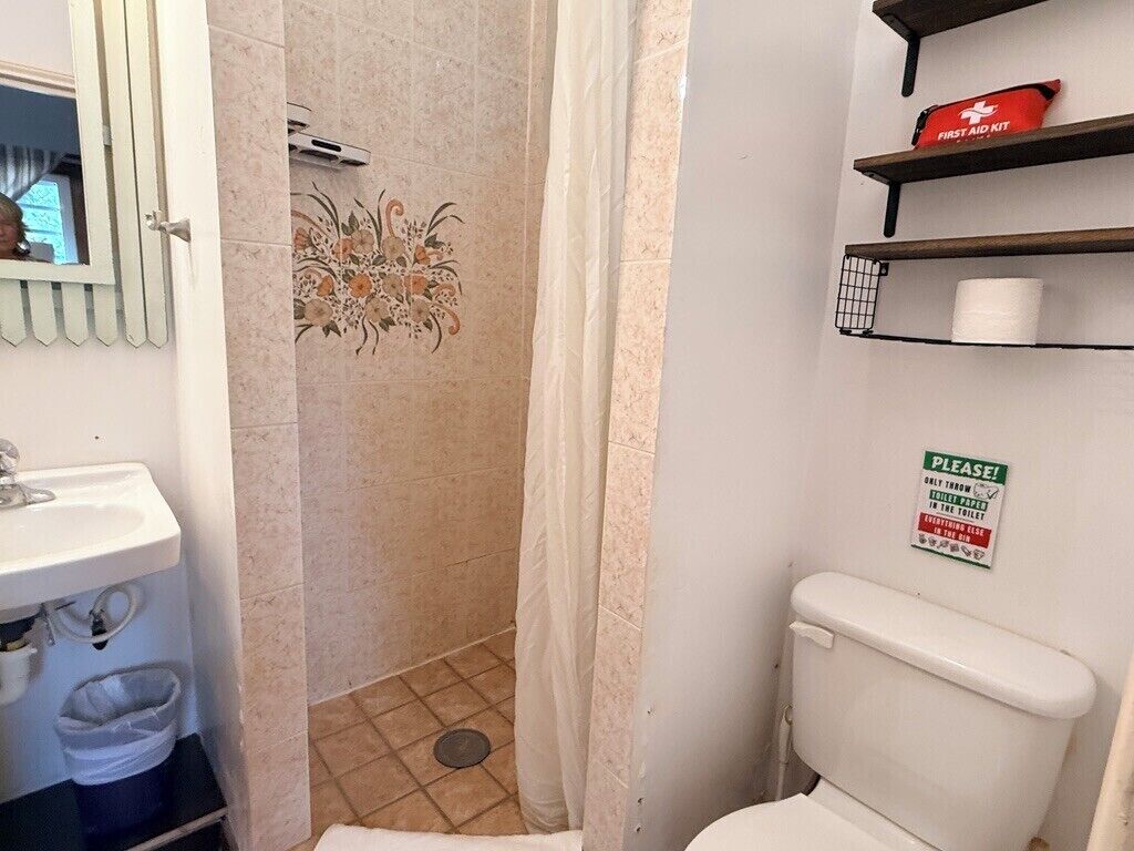 A bathroom with a toilet, a sink, a shower curtain, and a first aid kit on a shelf.