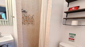 A bathroom with a toilet, a sink, a shower curtain, and a first aid kit on a shelf. - Cozy Room for the Budget Traveler in Maya Beach (Maya Beach)