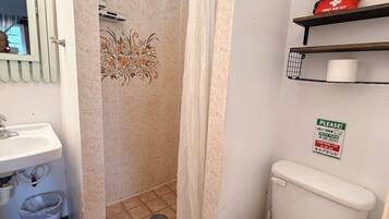 A bathroom with a toilet, a sink, a shower curtain, and a first aid kit on a shelf.