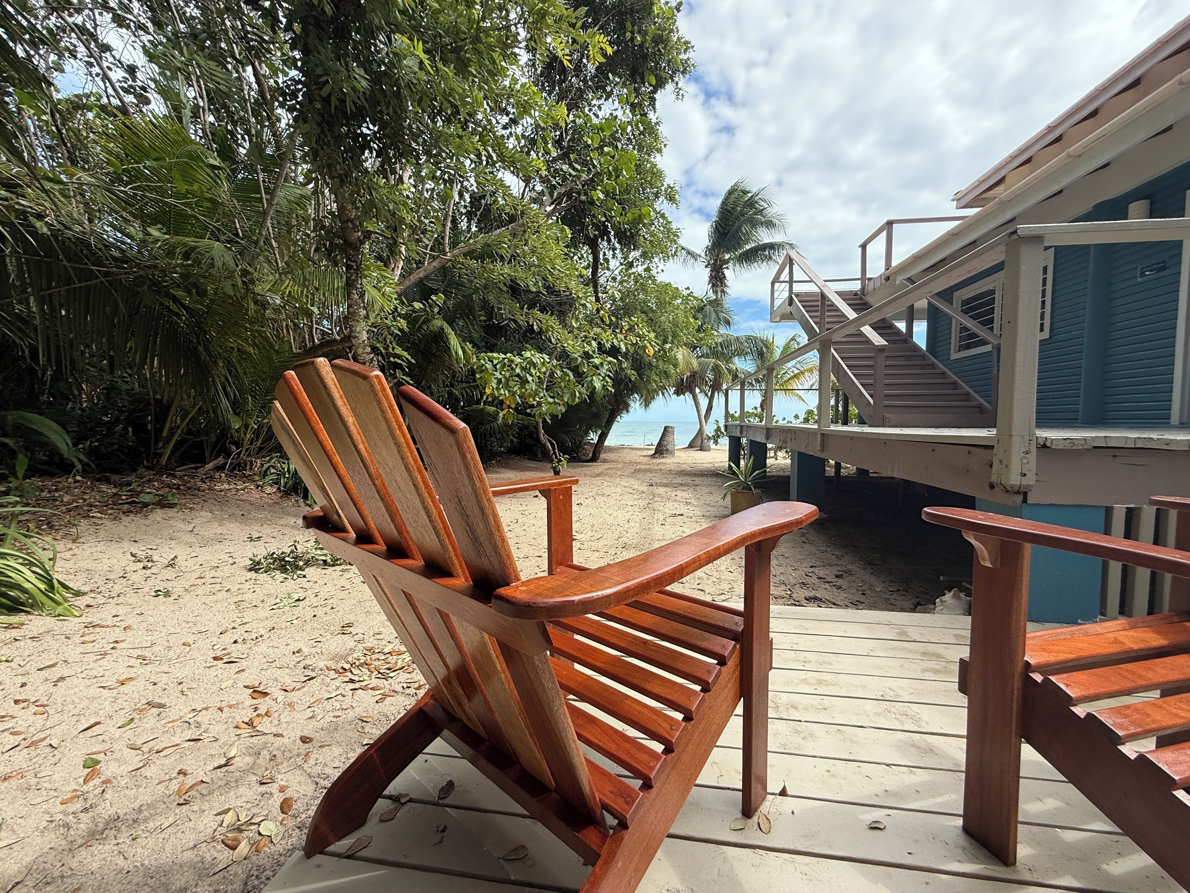 A wooden chair on a wooden deck with a view of a beach and palm trees.