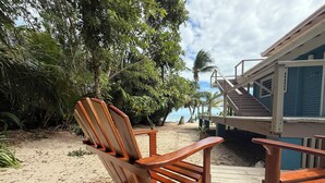 A wooden chair on a wooden deck with a view of a beach and palm trees. - Cozy Room for the Budget Traveler in Maya Beach (Maya Beach)