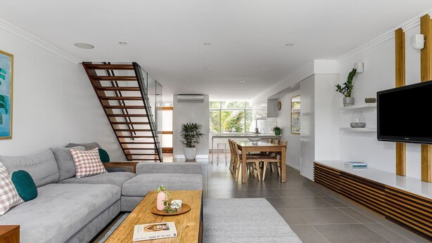 A modern living room with a grey sofa, wooden coffee table, and a staircase. - 1 James Cook Apartments - Opposite Clarkes Beach (Byron Bay)
