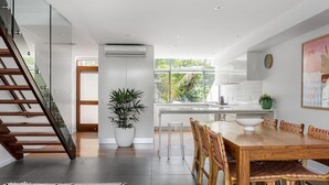 A modern kitchen with a large window, a dining area with wooden chairs, and a staircase. - 1 James Cook Apartments - Opposite Clarkes Beach (Byron Bay)