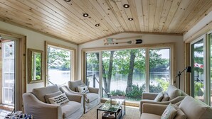 A cozy room with a wooden ceiling, large windows, and a view of a lake. There are two sofas and a coffee table. - All Day Sun! 7 bed 2 bath cottage on Lake Muskoka! Perfect Location! Privacy! (Torrance)