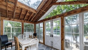 A wooden-paneled room with a large table and chairs, large windows, and a view of a body of water. - All Day Sun! 7 bed 2 bath cottage on Lake Muskoka! Perfect Location! Privacy! (Torrance)