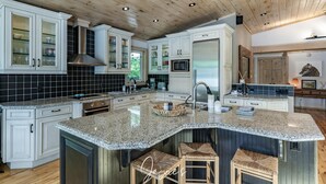 A spacious kitchen with granite countertops, white cabinetry, and a large island with stools. - All Day Sun! 7 bed 2 bath cottage on Lake Muskoka! Perfect Location! Privacy! (Torrance)