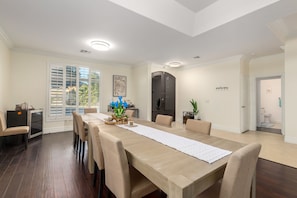Uma sala de jantar com uma mesa grande, cadeiras e vista para o exterior através de uma porta deslizante.