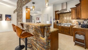 A modern kitchen with a stone accent wall, wooden cabinets, and a bar area with stools. - Phoenix Vacation Home -- Pool, Spa, Basketball & Putting Green (Phoenix)