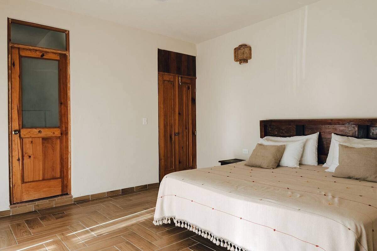 Een slaapkamer met een houten deur, een garderobe, een bed met een witte dekbedovertrek en een klein wandlampje.