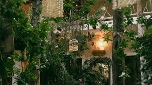 A courtyard with a thatched-roof structure, surrounded by lush greenery and hanging decorations.