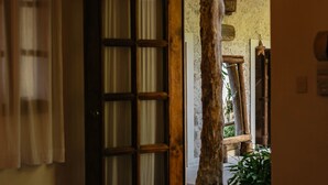 A room with a large wooden door leading to an outdoor area with a tree and a wooden bench.