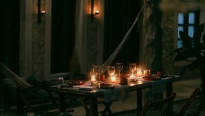 A dimly lit dining area with a table set for a meal, surrounded by chairs, and illuminated by candles.