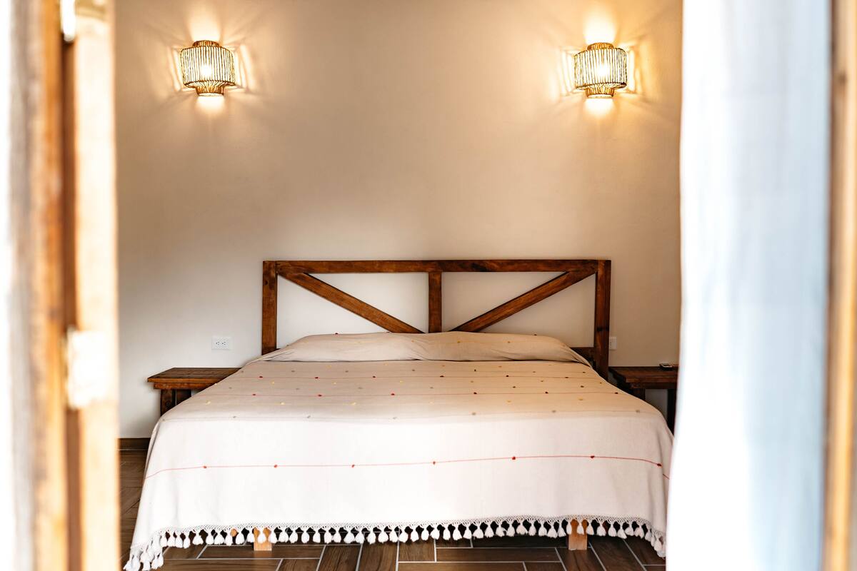 Een net opgemaakt bed met een houten hoofdbord, twee bedlampen en een witte deken.