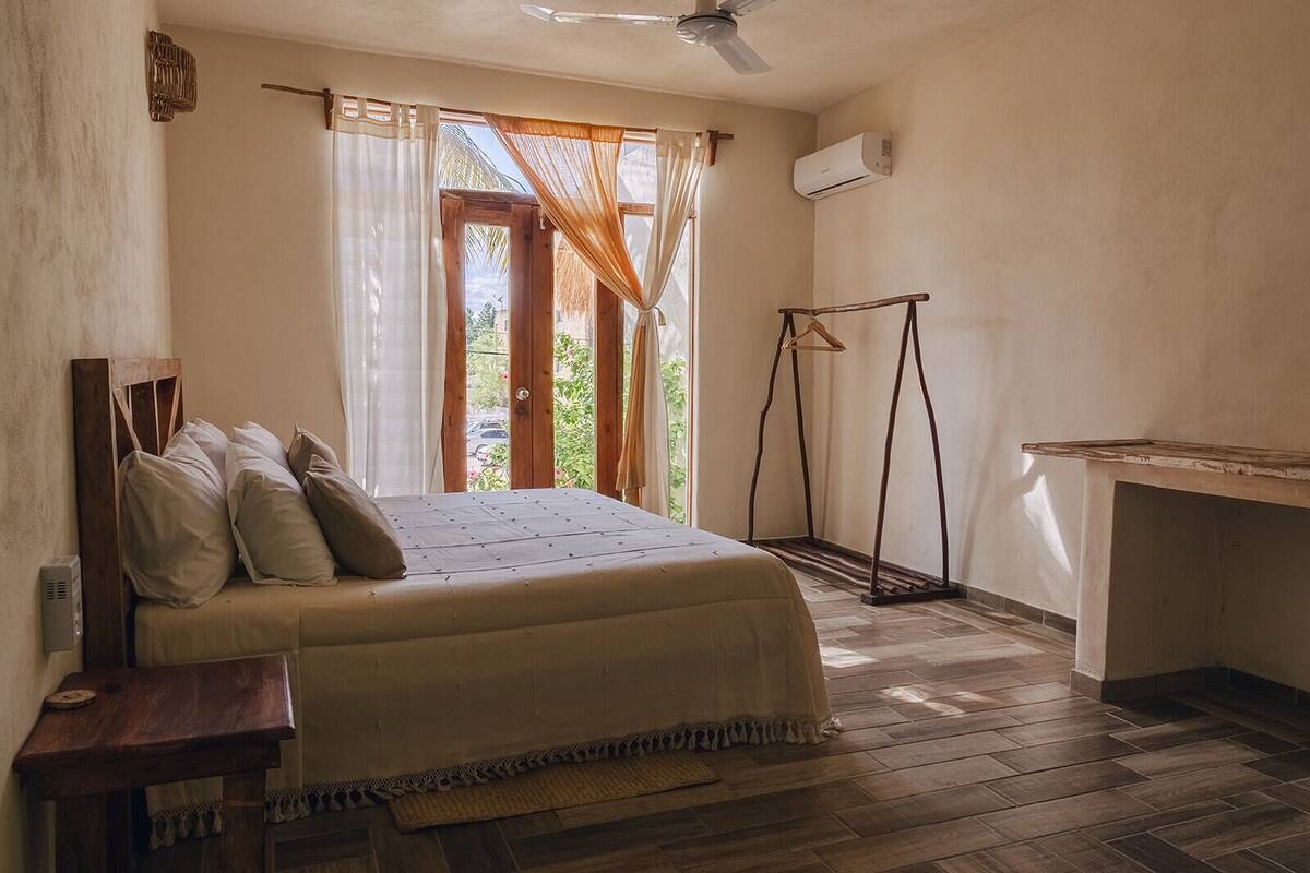 Een slaapkamer met een bed, een houten bureau, een kledingrek en een raam met gordijnen.
