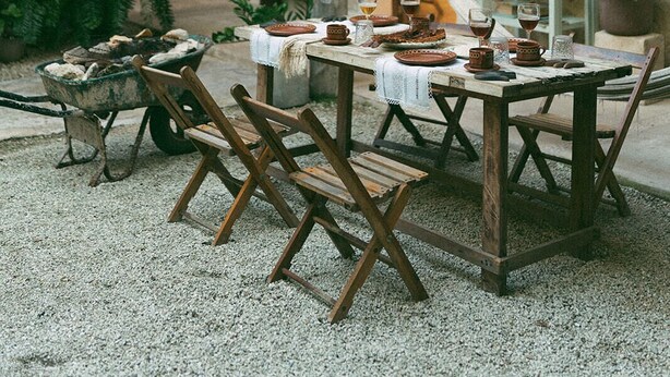 An outdoor dining area with rustic wooden tables and chairs, surrounded by potted plants and a stone wall.