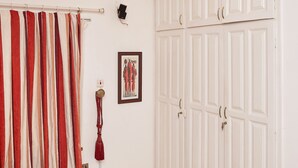 Een kamer met een wit plafond, een kroonluchter, een gordijn met rode en witte strepen, en een garderobe met meerdere deuren.